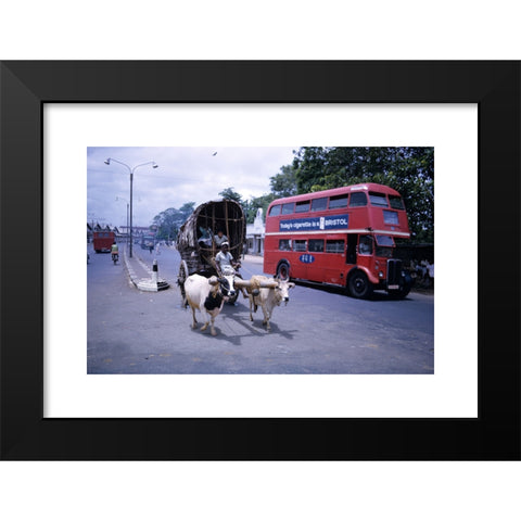 1960's Image Collection by James Davis Photography - Black Modern Wood Framed Art Print Titled: Old ox drawn cart and bright red ex London bus with Bristol cigarette advert on the side in mid 1960s in Colombo Sri Lanka