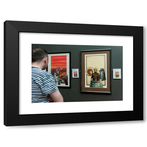 1960's Image Collection by Stephen Chung - Black Modern Wood Framed Art Print Titled: London, UK. 4 May 2016. A visitor views (L) 'Dinosaur Invasion' (1976) and (R) 'The Genesis of the Daleks' (1976) both by the artist Chris Achilleos. Doct