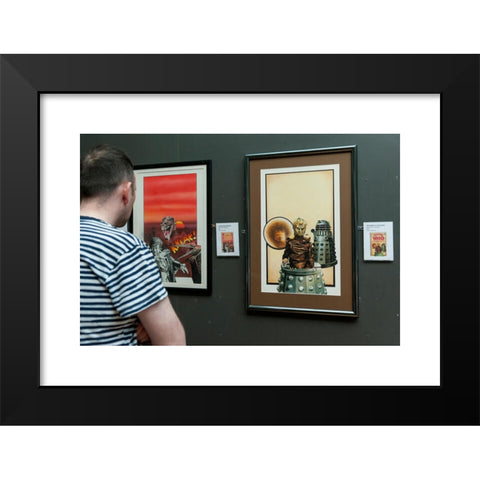 1960's Image Collection by Stephen Chung - Black Modern Wood Framed Art Print Titled: London, UK. 4 May 2016. A visitor views (L) 'Dinosaur Invasion' (1976) and (R) 'The Genesis of the Daleks' (1976) both by the artist Chris Achilleos. Doct